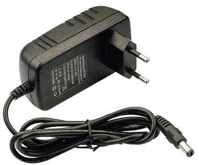 A imagem mostra uma fonte de alimentação (carregador) preta É um bloco retangular com dois pinos redondos (padrão europeu/brasileiro) para ligar na tomada. Um cabo preto fino sai do bloco, terminando em um conector cilíndrico (tipo barrel jack) para conectar ao dispositivo.