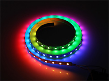 Uma fita de LED enrolada brilha em cores vibrantes sobre um fundo escuro. A luz forma um degradê suave, passando pelo vermelho, laranja, amarelo, verde, azul e roxo. Os pequenos pontos de luz criam um efeito de arco-íris luminoso e contínuo em formato de espiral.