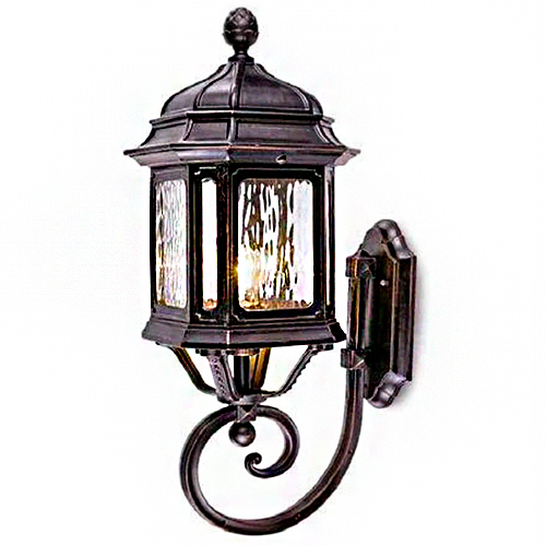 
Uma luminária de parede (arandela) clássica em metal escuro. Possui um formato de lanterna sextavada com vidros martelados, que criam um efeito ondulado. O topo tem um adorno de pinha e a base é sustentada por um braço metálico em formato de voluta (caracol) elegante. Estilo colonial