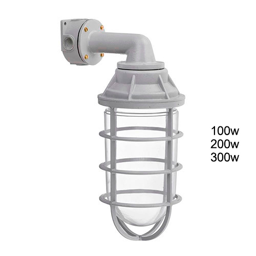 Esta imagem mostra uma luminária blindada industrial cinza fixada à parede por um braço em ângulo de 90 graus. A lâmpada fica protegida dentro de um vidro transparente em formato de cápsula, envolto por uma grade metálica de proteção. É um modelo robusto para uso técnico ou externo.