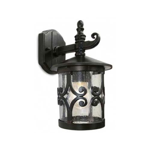 Arandela Externa Candile estilo colonial em metal preto. Possui formato cilíndrico com vidro transparente e detalhes decorativos em curvas (arabescos). O topo tem um chapéu circular com um detalhe pontiagudo. Uma lâmpada de luz quente brilha suavemente em seu interior.