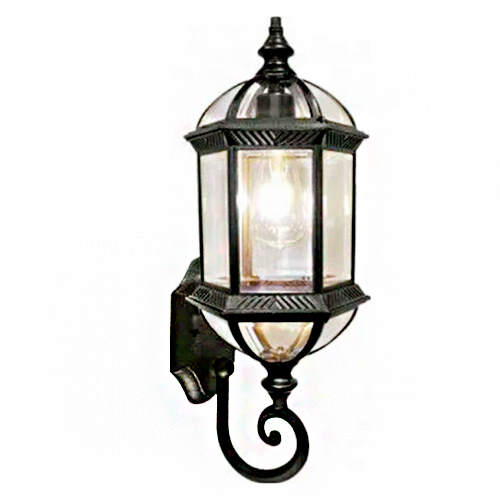 Esta imagem mostra uma arandela externa clássica. Ela tem formato sextavado (seis lados) com estrutura em metal preto e painéis de vidro transparente, revelando uma lâmpada acesa no interior. Possui um suporte de parede curvo e um detalhe decorativo em espiral na base.