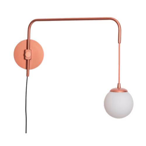 Esta arandela moderna tem uma base circular metálica em tom cobre rosado, fixada à parede. Dela sai uma haste fina que sobe e dobra-se em um ângulo reto, formando um braço horizontal. Na ponta, um fio curto sustenta um globo de vidro branco fosco, que pende como uma luminária pendente.