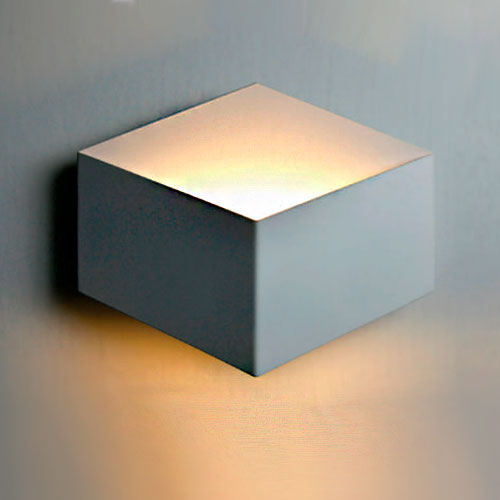 Arandela de parede em formato de cubo, com design moderno e minimalista. A luz sai suavemente pela parte superior e inferior, criando um efeito indireto e aconchegante na parede em tom claro.