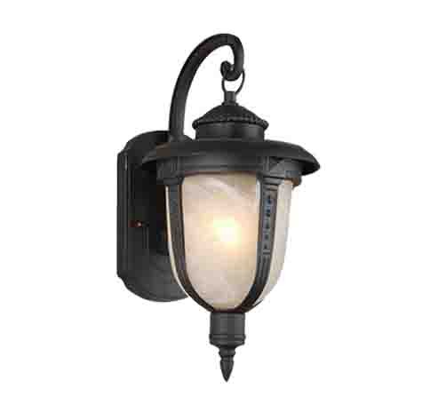 É uma arandela colonial de parede, na cor preta, com formato de lanterna antiga. Tem topo arredondado, laterais com vidro fosco que suaviza a luz, e um braço curvo que a sustenta. A luminária aponta levemente para baixo e tem detalhe pontiagudo na parte inferior