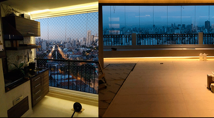 Lado Esquerdo: Mostra uma sacada menor, com uma área gourmet (armários de madeira e bancada) e protegida por uma rede de segurança. A foto é noturna, com as luzes da cidade e dos carros iluminando a paisagem. Lado Direito: Mostra uma varanda muito mais ampla, fechada com painéis de vidro (tipo "cortina de vidro"). O piso é claro e a iluminação é feita por uma fita LED que percorre a base da janela, criando um ambiente moderno. A vista da cidade é ampla, no final da tarde ou início da noite.