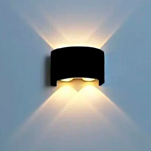 
Esta arandela combina o rústico e o moderno. Possui uma base redonda de madeira clara e um braço metálico preto que sustenta uma cúpula em formato de meia esfera. O acabamento externo é preto fosco, enquanto o interior é acobreado, criando um contraste elegante e acolhedor na iluminação.