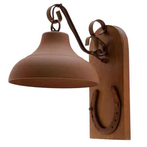 
Arandela rústica de parede. Sobre uma base de madeira vertical, há uma ferradura de metal na parte inferior. Do topo, sai um braço metálico curvado que sustenta uma luminária em formato de sino na cor marrom-fosco. O estilo é colonial e campeiro.