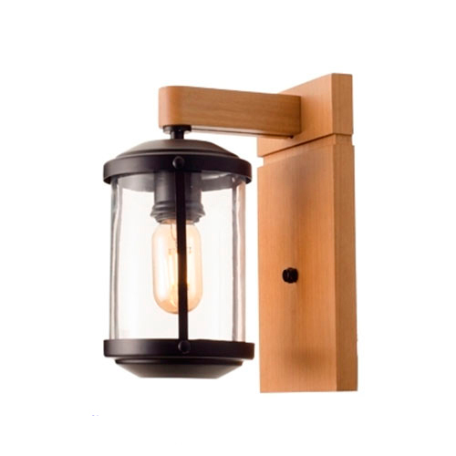 Uma arandela de parede elegante que mistura o rústico e o industrial. Possui uma base vertical e braço em madeira clara, sustentando uma lanterna cilíndrica de vidro transparente com detalhes em metal preto. No centro, uma lâmpada de filamento aquece o ambiente.