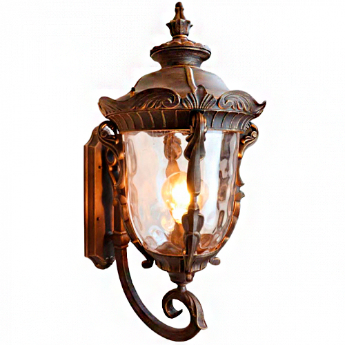 Uma arandela externa de parede em estilo clássico e colonial. É feita de metal com acabamento em ouro envelhecido, possui detalhes ornamentais esculpidos e uma cúpula de vidro jateado ondulado. No centro, uma lâmpada acesa emite uma luz quente e acolhedora.