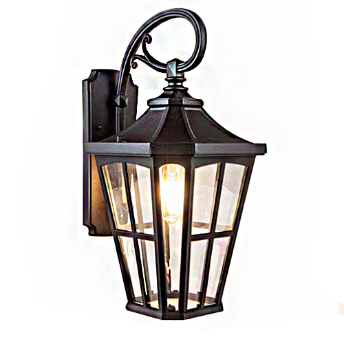 Esta imagem mostra uma arandela de parede clássica em estilo lanterna colonial. Ela é feita de metal preto com um braço curvado em forma de "S" no topo. O corpo tem formato sextavado com vidros transparentes, revelando uma lâmpada interna que emite uma luz amarela e quente