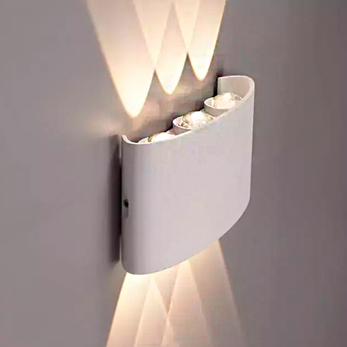 
Esta arandela branca tem um design curvo e moderno, assemelhando-se a um escudo ou uma letra "C" alongada fixada à parede. Ela possui três pontos de LED no topo e na base, projetando múltiplos feixes de luz cruzados que criam um efeito artístico de triângulos luminosos para cima e para baixo