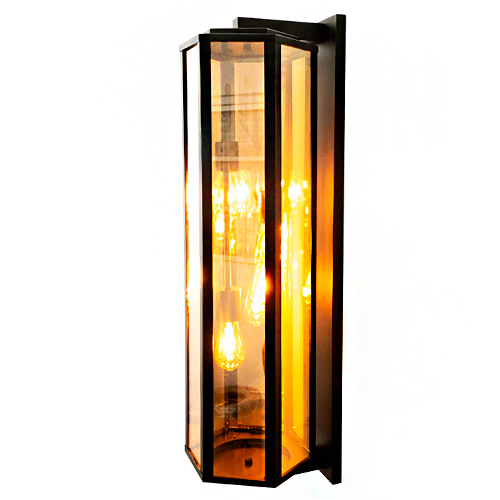 Uma arandela vertical alongada com estrutura metálica preta e formato hexagonal. Possui paredes de vidro transparente que revelam cinco lâmpadas de filamento em seu interior. A luz emitida é um amarelo quente e brilhante, criando um visual elegante, rústico e acolhedor.