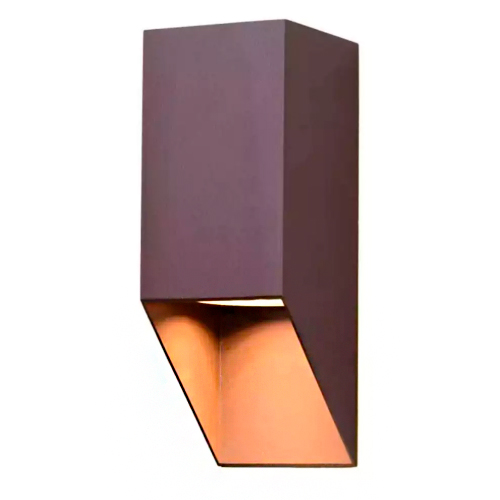 Esta arandela possui um design geométrico e minimalista, assemelhando-se a um bloco retangular de cor marrom. A base inferior é cortada em diagonal, revelando um interior acobreado que reflete uma luz quente e suave para baixo, criando um efeito decorativo moderno.