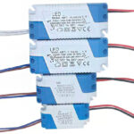 A imagem mostra quatro fontes (drivers) para LED empilhadas. São caixas retangulares, brancas e azuis. Têm especificações impressas, como tensão de entrada ("Input: 110V−220V"), saída ("Output: 45V−84V / 280−300mA"), e modelos como "ABT-15-24X1W". Fios elétricos coloridos (vermelho, preto, branco/azul) saem delas.